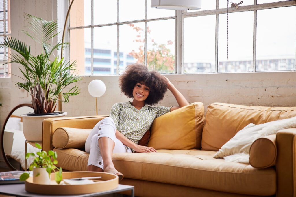 Mulher jovem sorridente relaxando em um sofá confortável em casa à tarde.