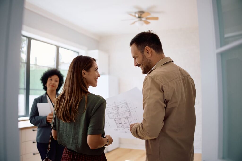 Casal com um projeto do apartamento na mão e uma arquiteta ao fundo