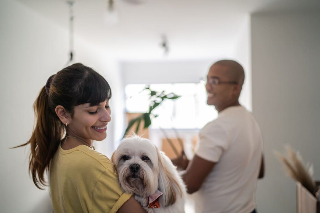 Casal entrando em um apartamento durante o dia com a mulher segurando um cachorro no colo.