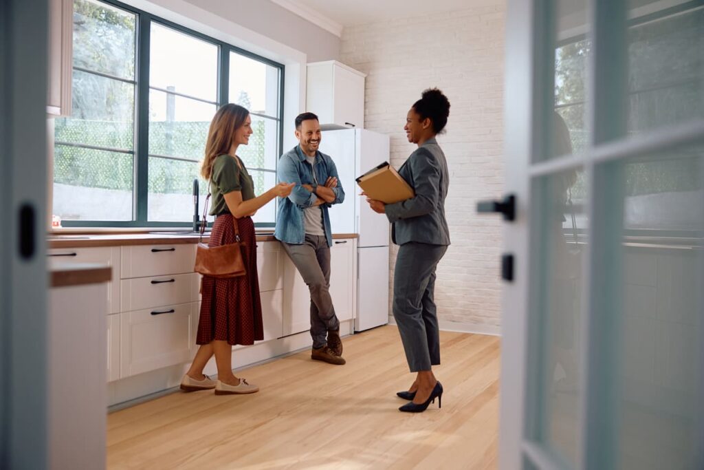 Um casal e uma corretora de imóveis conversando e sorrindo dentro de um apartamento. 