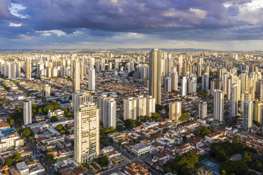 Imagem aérea da cidade de São Paulo em dia ensolarado mas com algumas nuvens carregadas no céu.