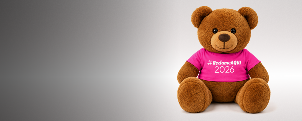 Urso de pelúcia mascote do Reclame AQUI usando camiseta rosa com o texto #ReclameAQUI 2026, ilustrando o Prêmio Reclame AQUI 2026 em que a Housi é finalista